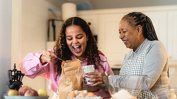 young girl and older woman smiling whilst preparing food in a kitchen environment